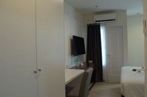 A hotel room with a bed, a desk with a chair, a television, and an air conditioning unit. - Giia Sanno Menteng (Jakarta)