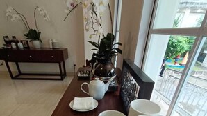 A dining area with a wooden table set with white plates, cups, and a teapot. There are orchids on the wall and a view of the outside through a window. - Giia Sanno Menteng (Jakarta)