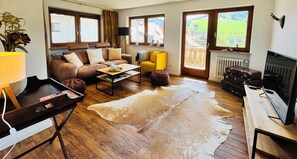 A living room with a brown leather sofa, a yellow armchair, a coffee table, and a large window with a view of greenery. - Recreation resort for Black Forest fans (Horben)