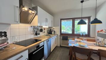 A modern kitchen with a built-in oven, a dining area with a table and chairs, and a window with a view of greenery.