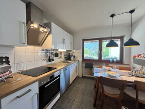 A modern kitchen with a built-in oven, a dining area with a table and chairs, and a window with a view of greenery. - Recreation resort for Black Forest fans (Horben)