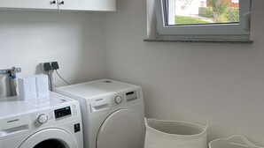 A laundry room with two white Samsung washing machines, a window with a view of greenery, and two woven baskets. - Recreation resort for Black Forest fans (Horben)