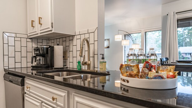 A modern kitchen with white cabinetry, a black countertop, and a stainless steel sink. - Long Drive On No. 5 - 1BR Condo w/ GREAT Golf Views, Minutes From Clubhouse (Pinehurst)