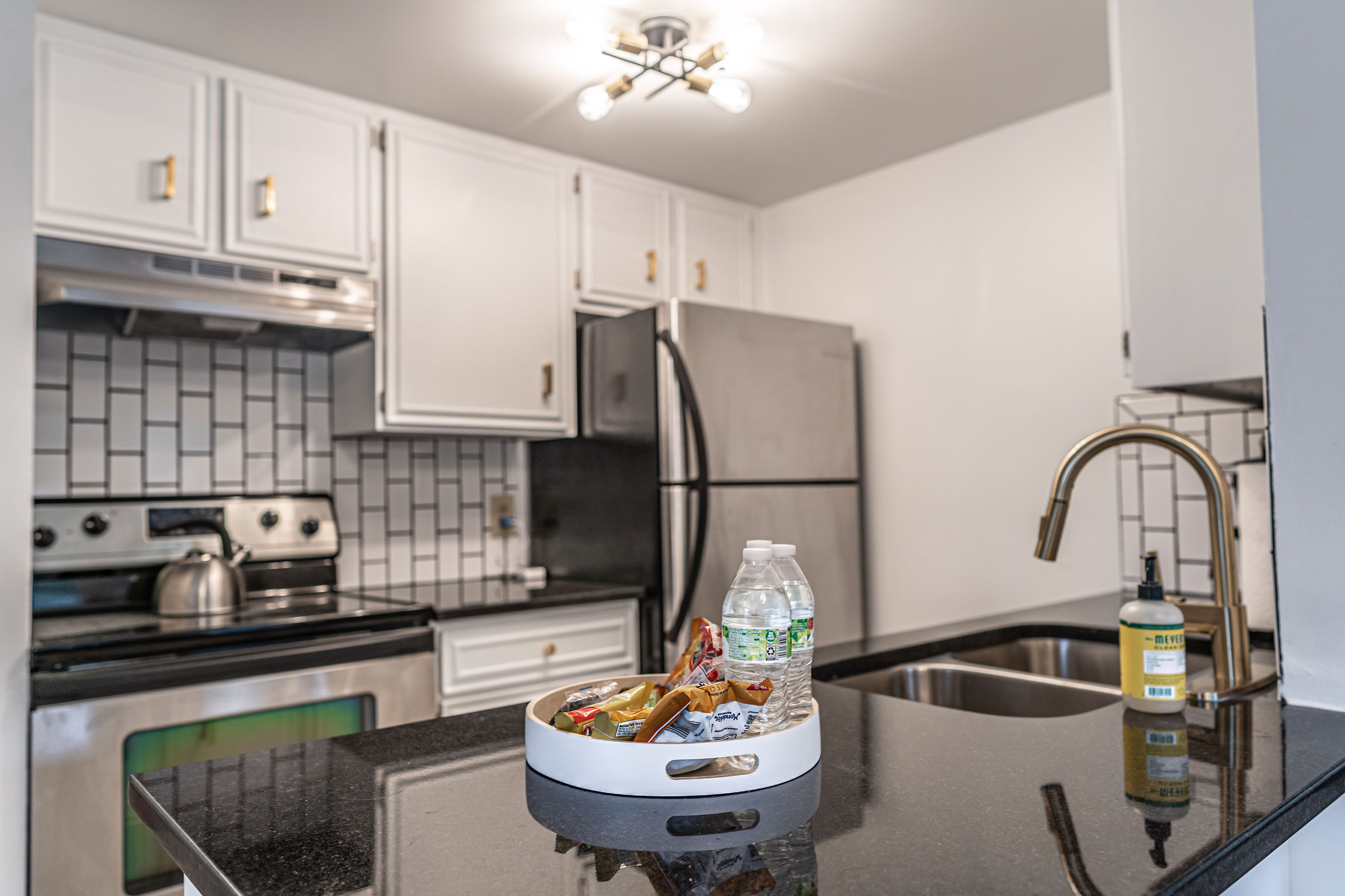 Une cuisine avec des armoires blanches, un réfrigérateur en acier inoxydable, une cuisinière et un évier.
