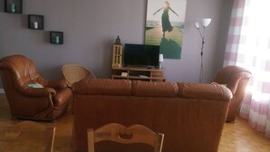 Uma sala de estar com sofá, cadeiras, televisão e um quadro na parede.
