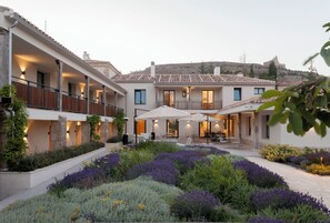 Un patio con piscina, rodeado de un jardín con flores moradas y un edificio de techo con tejas.