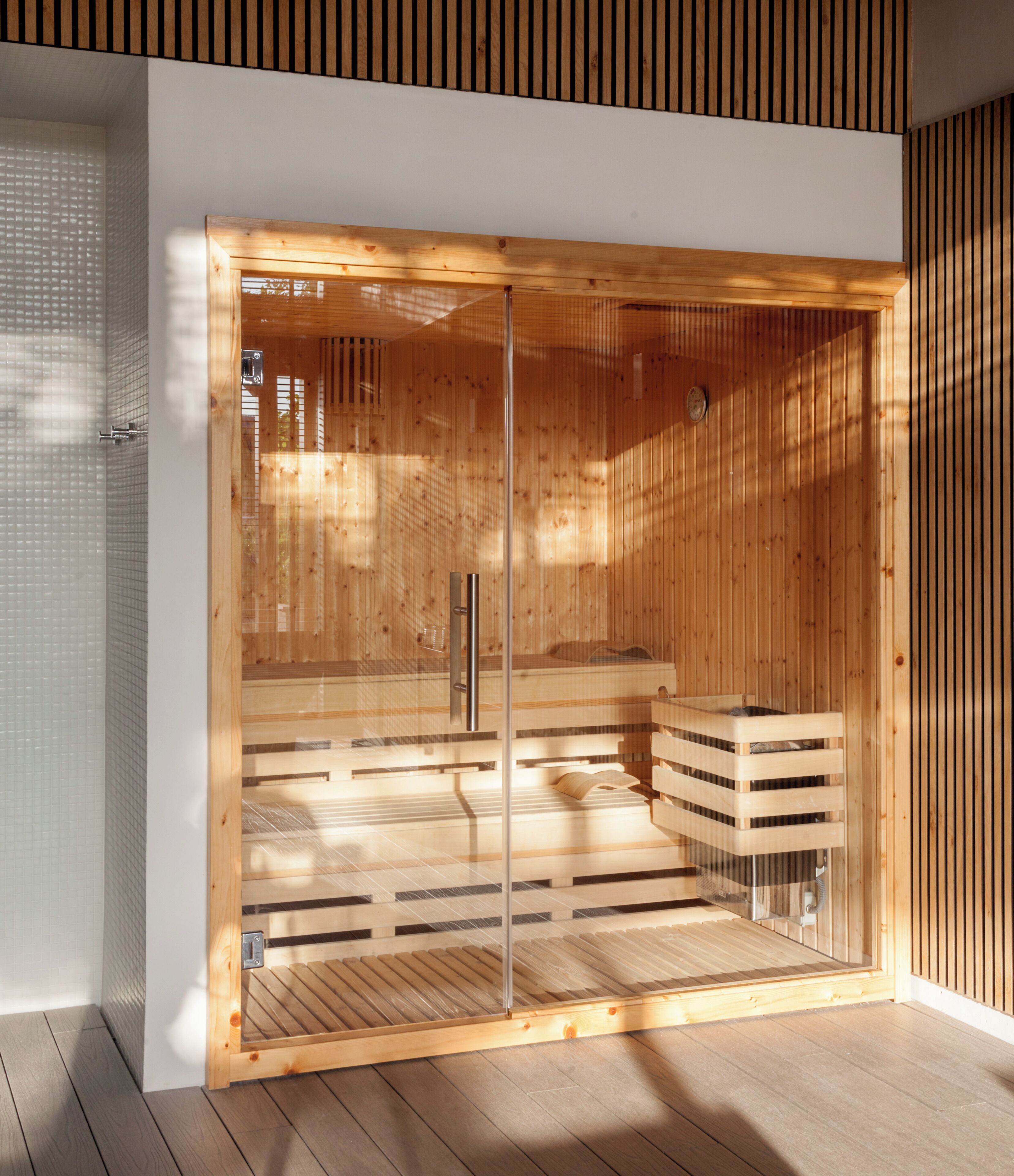 A sauna with wooden walls and a glass door, featuring a bench and a small wooden cabinet.