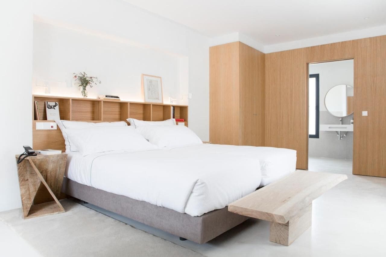 A modern bedroom with a bed, bedside tables, a wooden bench, and a minimalist design.