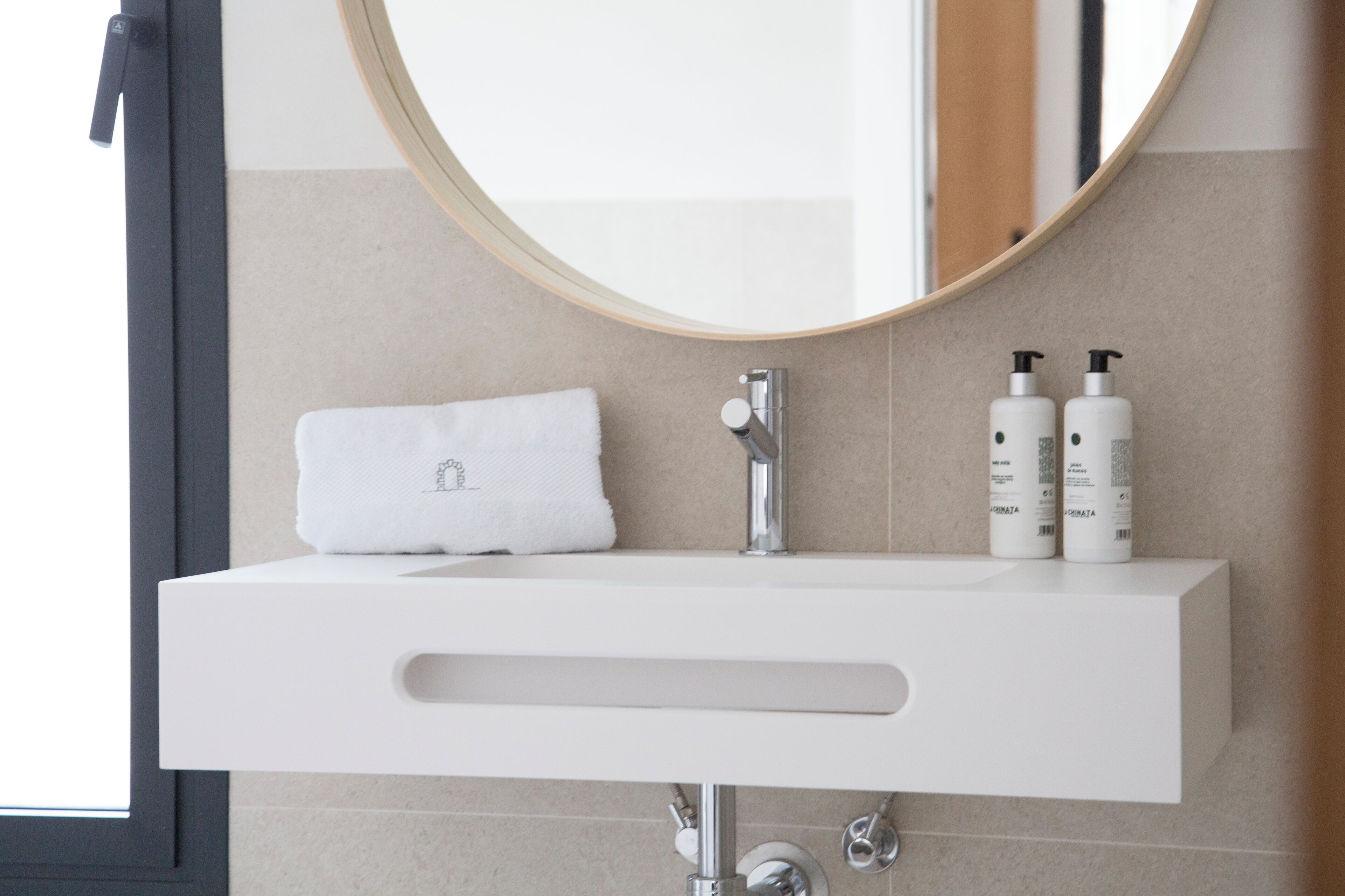 Un baño moderno con un lavabo blanco, un espejo redondo y dos botellas de artículos de aseo.