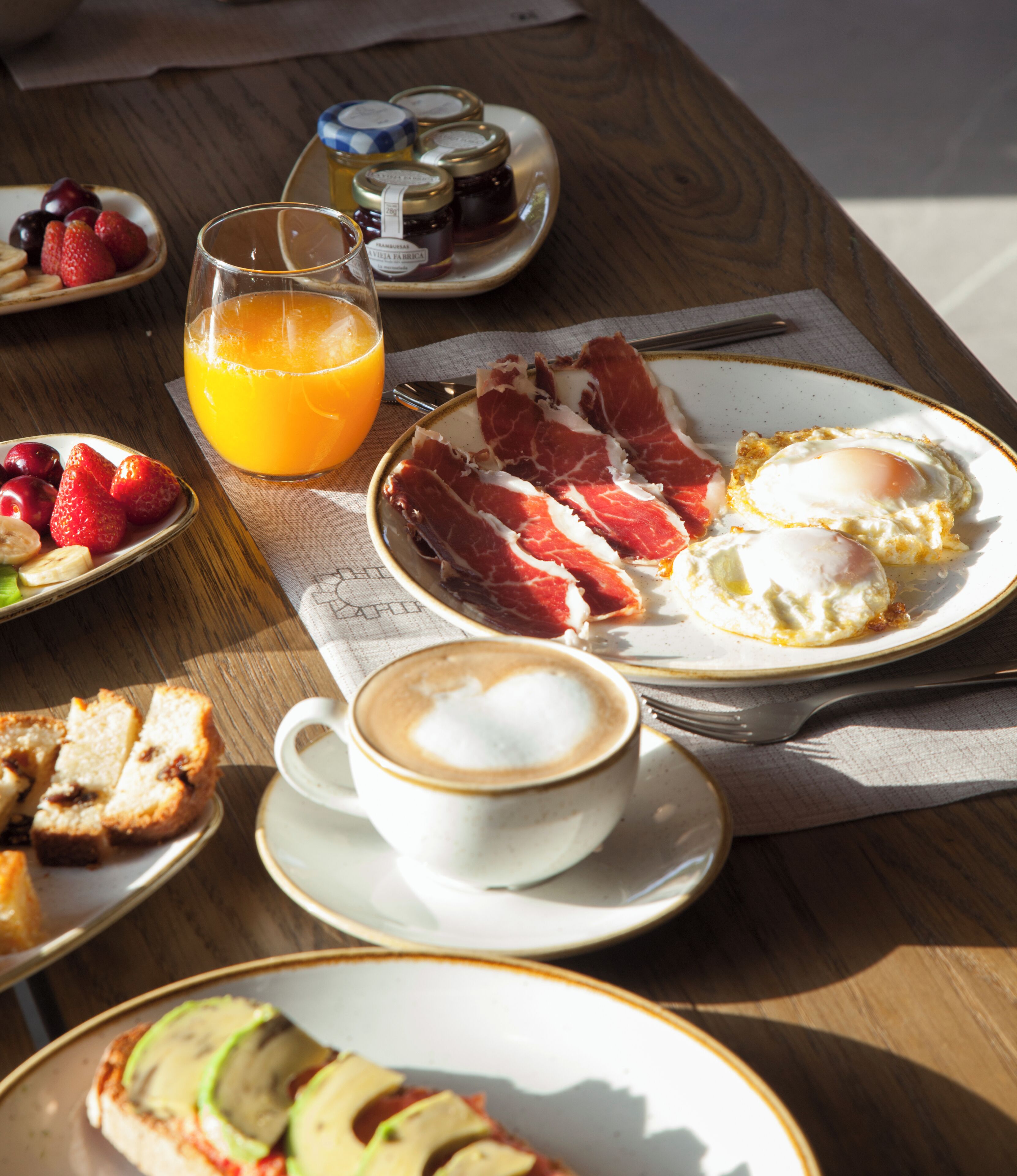 Una mesa de desayuno con platos de comida, un vaso de jugo de naranja y una taza de café.