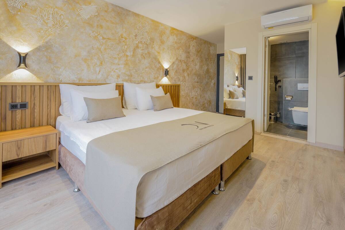 Quarto de hotel moderno com uma cama grande, cabeceira de madeira, mesas de cabeceira e um chuveiro amplo.