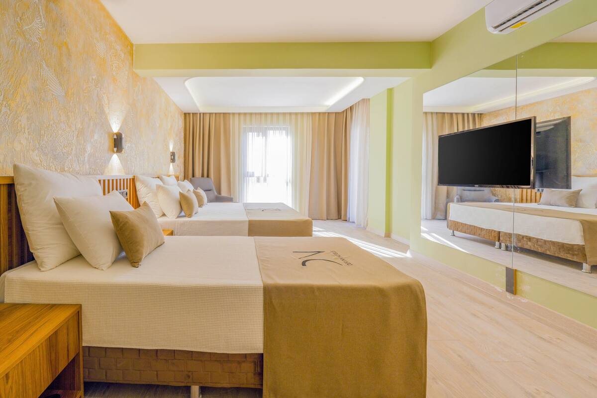 Quarto de hotel com uma cama grande, uma cama menor, um sofá-cama, uma televisão e uma escrivaninha.