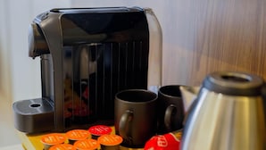 Kahvinkeitin, kaksi mukia, vedenkeitin ja erilaisia kahvikapseleita tarjottimella.