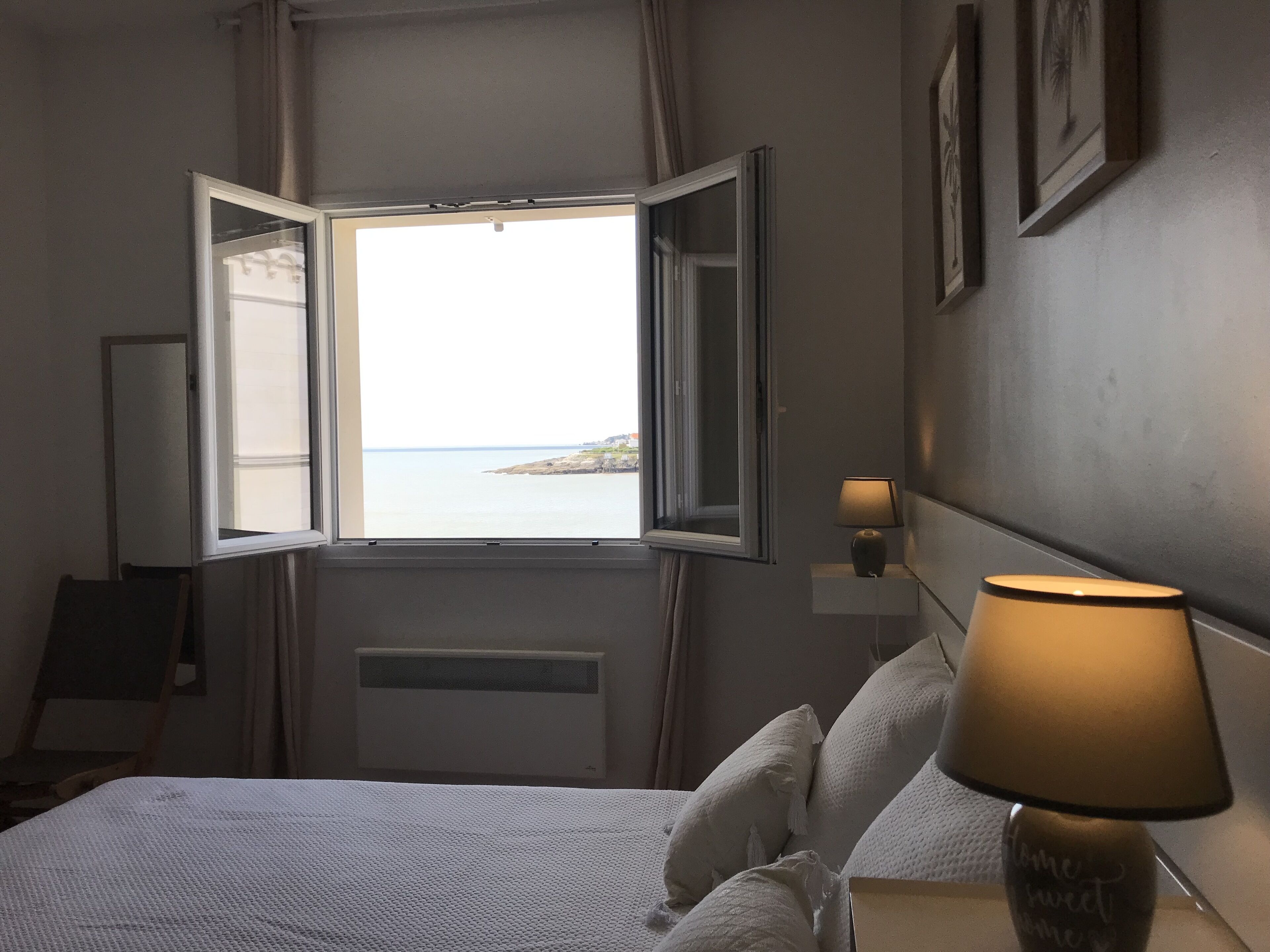 Une chambre d’hôtel avec un lit, une fenêtre donnant sur la mer, une lampe de chevet et une table de chevet fixée au mur.