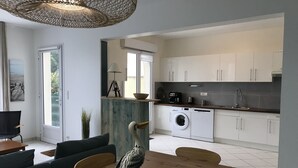 A modern kitchen with white cabinets, a washing machine, and a dining area with a wooden table and chairs.