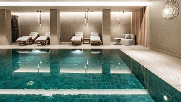 A modern indoor swimming pool with lounge chairs and a small seating area. - AC Hotel By Marriott St. Julian's (St. Julian's)