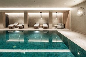 Piscina interior moderna con sillones de descanso y una pequeña zona de estar.