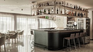 A modern bar area with a curved counter, multiple shelves of liquor bottles, and a seating area with chairs and tables. - AC Hotel By Marriott St. Julian's (St. Julian's)