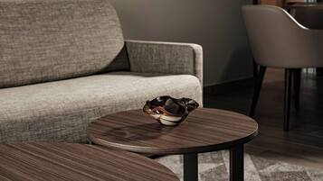 Een moderne woonkamer met een grijze bank, een ronde houten salontafel en een decoratieve glazen schaal.