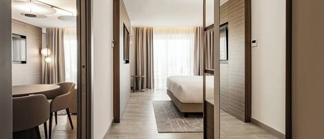A modern hotel room with a bed, a desk with chairs, a small table, and a mirror.
