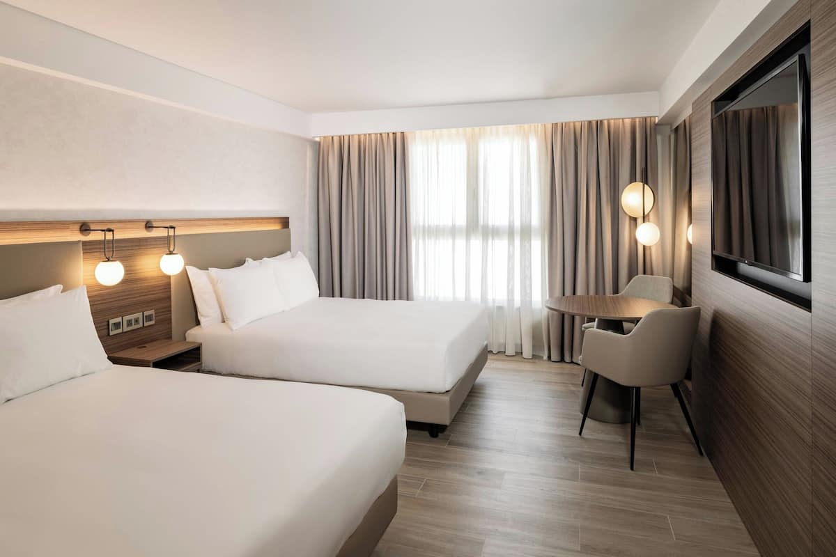 A hotel room with two beds, a desk, a chair, a TV, and curtains.