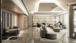 A modern living room with a sectional sofa, armchairs, and a coffee table. The room has a large window, a fireplace, and a bookshelf. - AC Hotel By Marriott St. Julian's (St. Julian's)