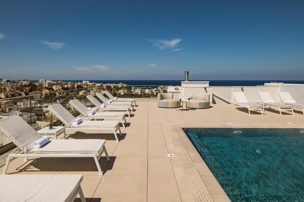 Zona de piscina en la azotea con tumbonas y vistas a la ciudad y al mar.
