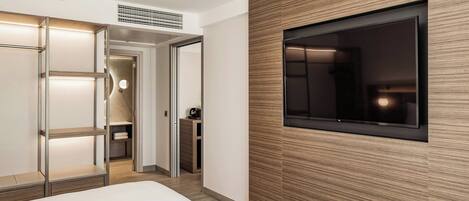 Una habitación de hotel moderna con una cama, un armario con puertas correderas, televisión integrada y sistema de ventilación en el techo.