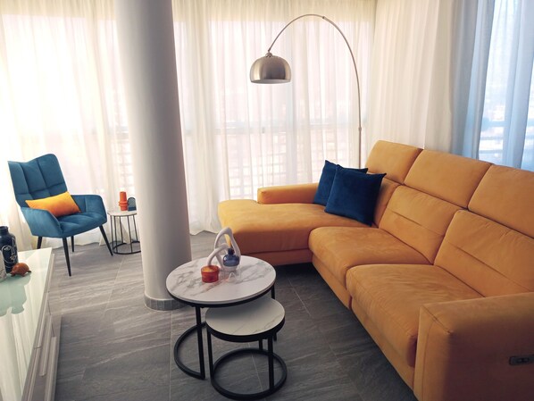 Un salon moderne avec un fauteuil bleu, un canapé orange, une table basse ronde et un lampadaire.