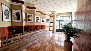 A spacious hallway with a tiled floor, framed photographs on the walls, and a potted plant.