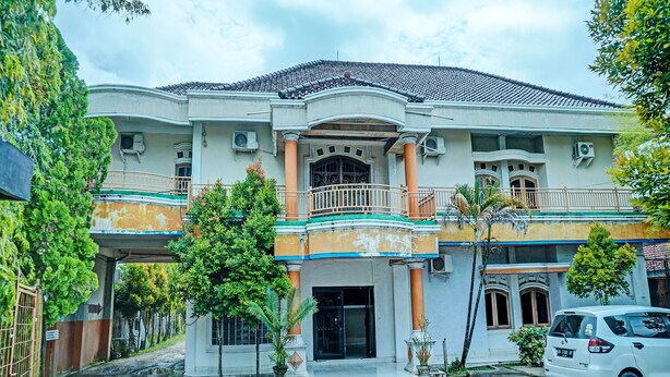 A multi-story building with a central entrance, balconies, and a car parked in front. - Hotel O Romli (Kayu Agung)