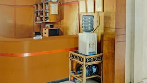 A reception area with a wooden counter, a water dispenser, a small refrigerator, and a shelf with various items. - Hotel O Romli (Kayu Agung)