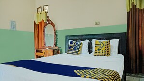A neatly made bed with a blue and yellow patterned bedspread, two pillows with blue and yellow designs, and a wooden dresser with a mirror. - Hotel O Romli (Kayu Agung)
