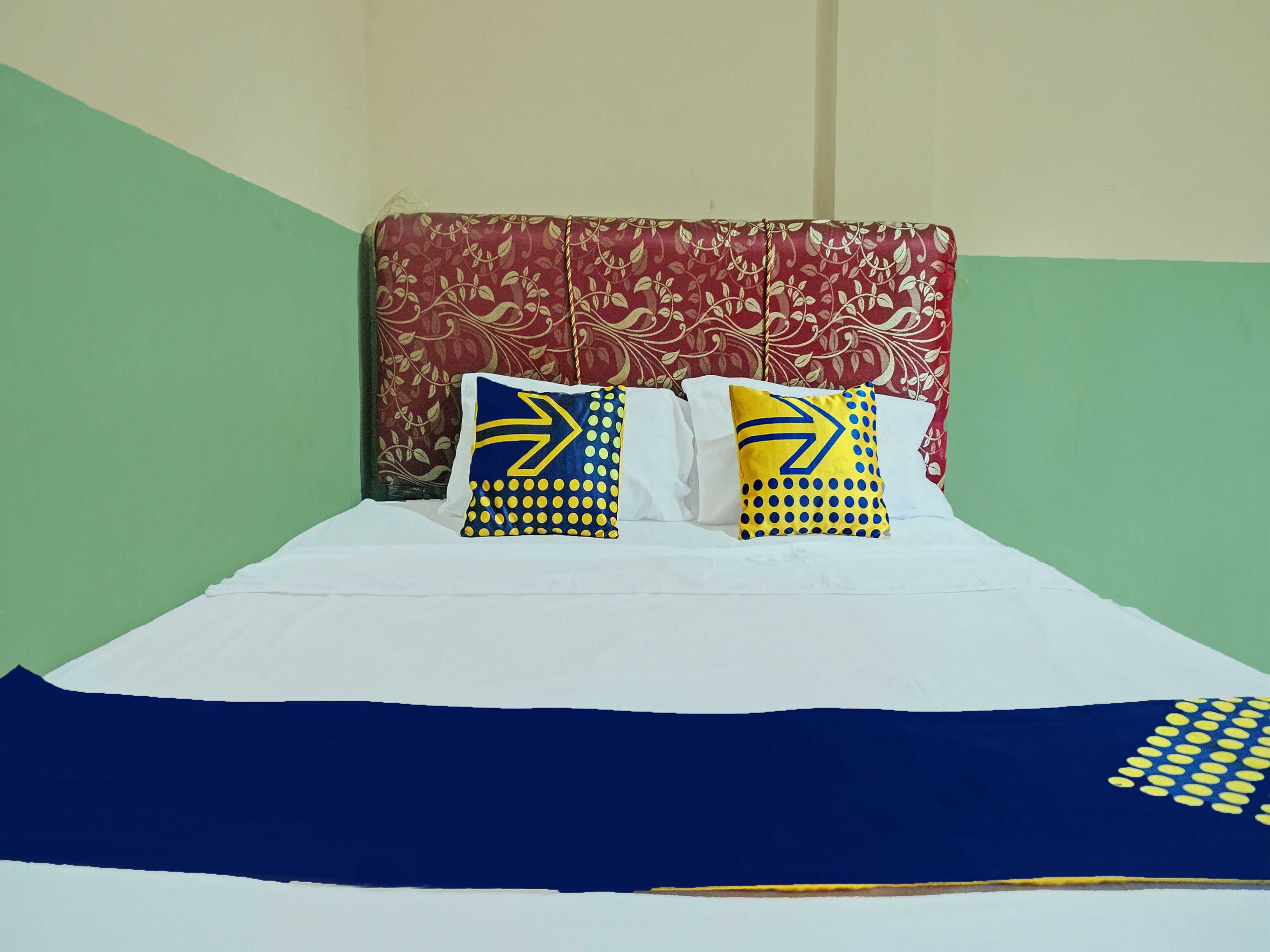 Una cama con sábanas blancas y dos almohadas con diseños azules y amarillos.