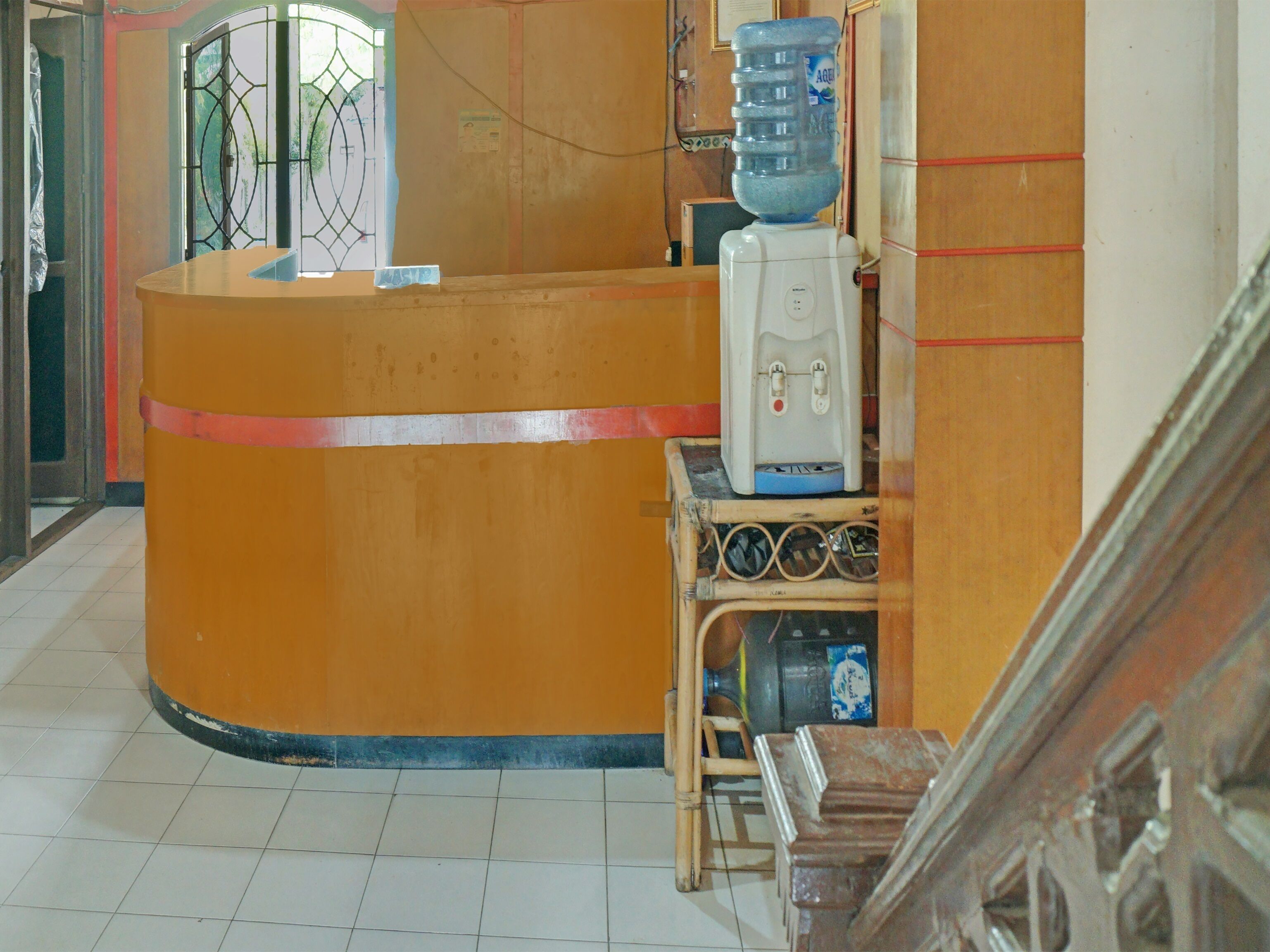 Ein Empfangsbereich mit einer gebogenen, orangefarbenen Theke, einem Wasserspender und einem kleinen Tisch mit Stuhl.