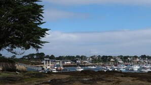 Uma marina costeira com barcos atracados, uma ponte e casas ao fundo.