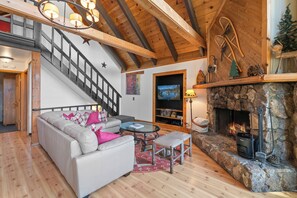 Un salon chaleureux avec une cheminée, un canapé, une table basse et un escalier.