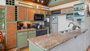 Una cocina con armarios verdes, encimera de granito, microondas, estufa, refrigerador y lavaplatos.