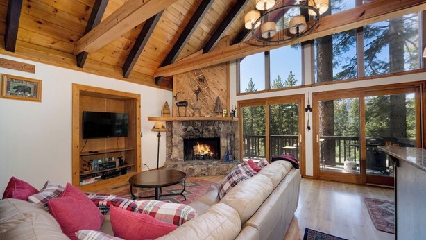 Una sala de estar acogedora con una chimenea de piedra, un sofá grande con cojines escoceses, un televisor y un techo de madera.