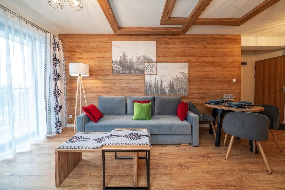 A modern living room with a grey sofa, wooden walls, and a dining table set for four.