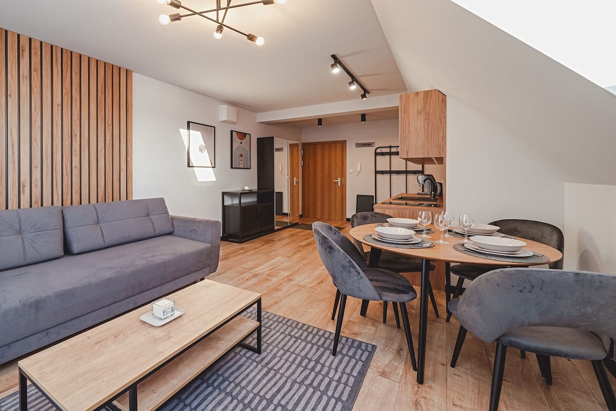 A modern living room with a grey sofa, a wooden coffee table, and a dining area with a round table set for four.