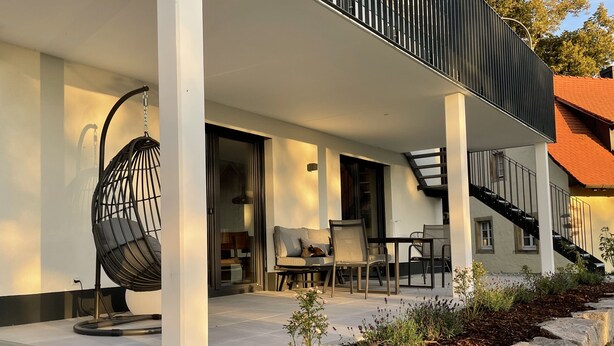Un espacio al aire libre moderno con un sillón colgante, un sofá y una mesa.