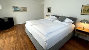 Una cama bien tendida con sábanas blancas, un cabecero gris y dos lámparas de noche.