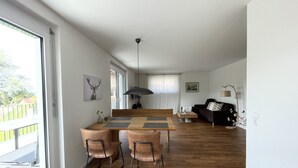 Un amplio salón con una mesa de comedor de madera, dos sillas, un sofá y un ventanal grande.