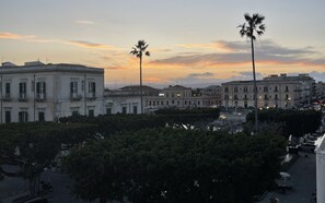 A cityscape at sunset with classical architecture, palm trees, and a clear sky.