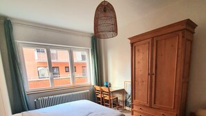 Een slaapkamer met een bed, een houten garderobe, een bureau met stoel en een raam met gordijnen.