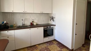 Een keuken met witte kastjes, een roestvrijstalen spoelbak en een gele hanglamp.