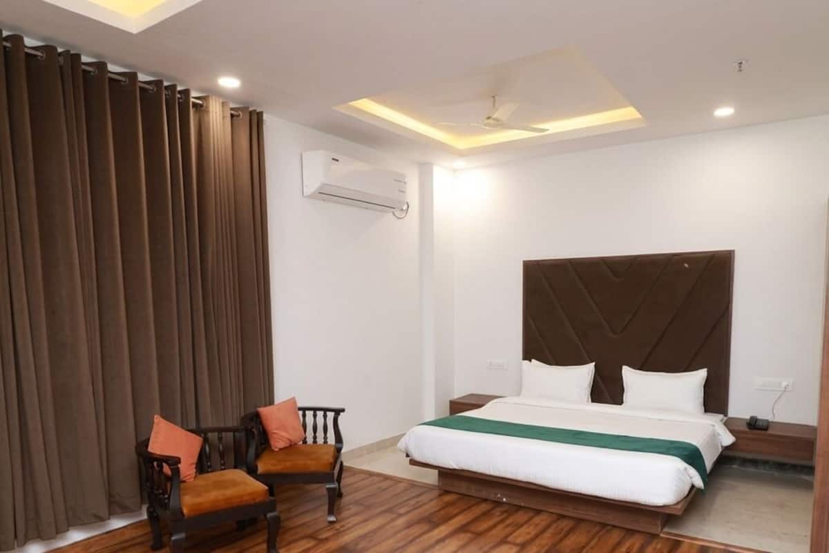 Une chambre dâhĂŽtel comprenant un lit, deux chaises, un ventilateur de plafond, un appareil de climatisation et un plancher en bois.