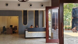 Una recepción con dos empleados, un interior moderno con paneles verticales y vistas al exterior.