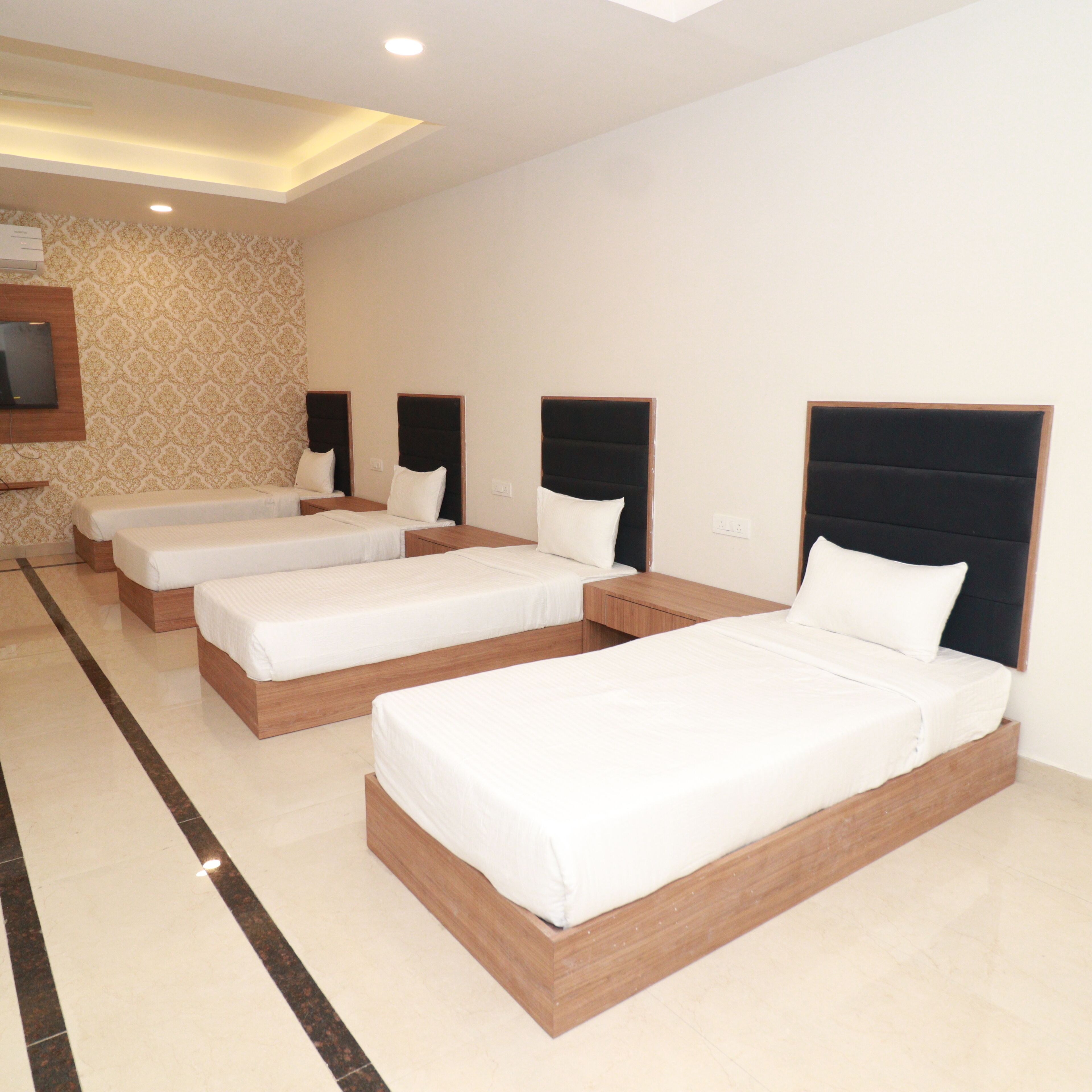 A hotel room with four single beds arranged in a row, each with a wooden frame and white bedding.